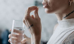 Eine junge Frau mit Tattoos schluckt eine Pille.