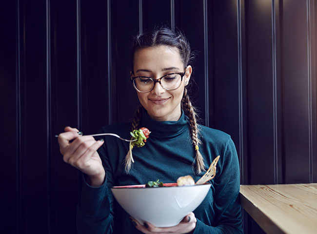 Eine Medizinstudentin hat einen gesunden Salat zubereitet und isst diesen.